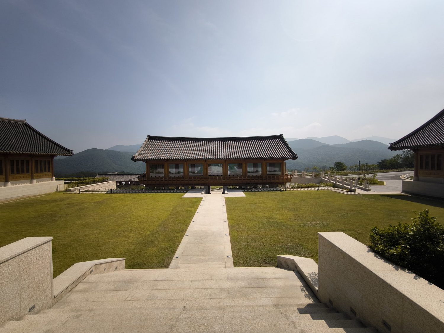 A hanok pavilion on a green lawn beneath the mountains